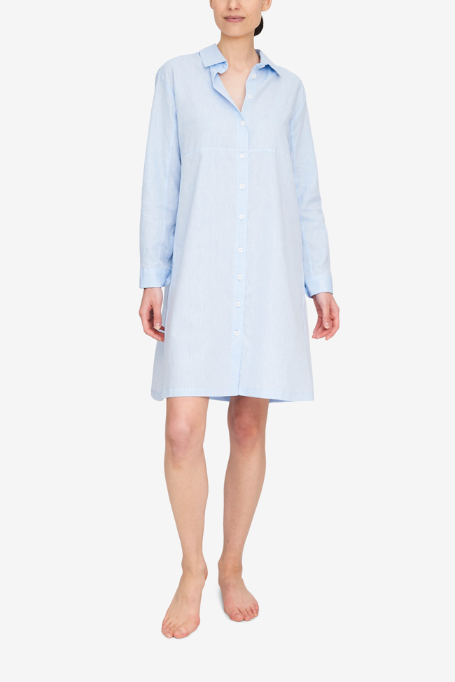 A woman wears the Button Down Sleep Shirt, with a full length placket. It hits at about the knee, and can be worn for sleep as well as a day dress. The light blue linen cotton blend fabric is timeless and chic.